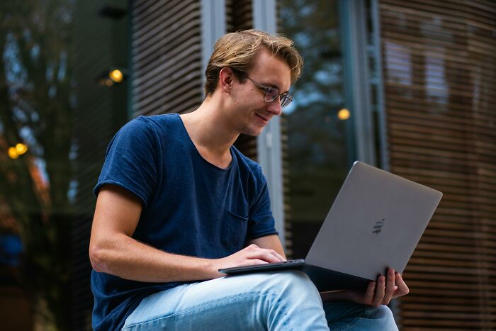 Gen Zer in blue shirt using laptop outdoors, likely sharing thoughts on boomer complaints.