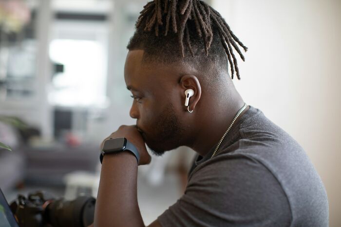 Young man wearing earbuds and smartwatch, deep in thought, possibly reflecting on Gen Z's boomer complaints.