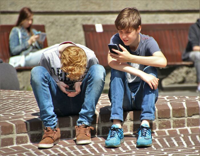 Two Gen Z individuals sitting on steps, focused on their smartphones.