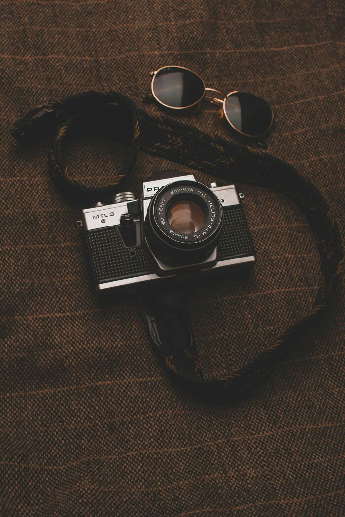 Retro camera and sunglasses on a brown textured background, evoking a nostalgic vibe.