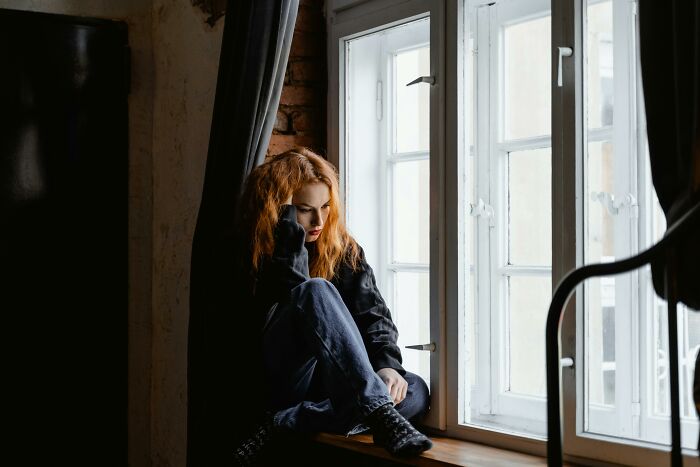 Gen Zer sitting by a window, looking contemplative, possibly reflecting on boomer complaints.