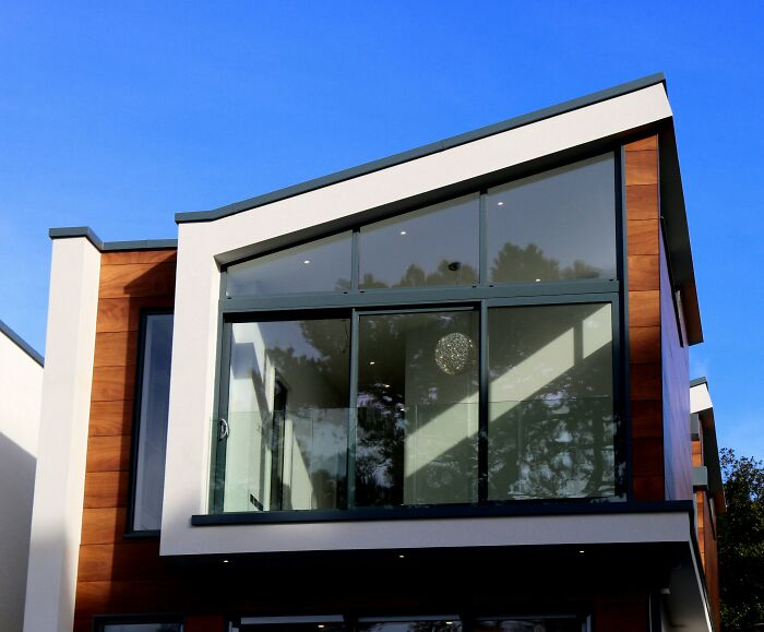 Modern house with large glass windows and wood accents under a clear blue sky.