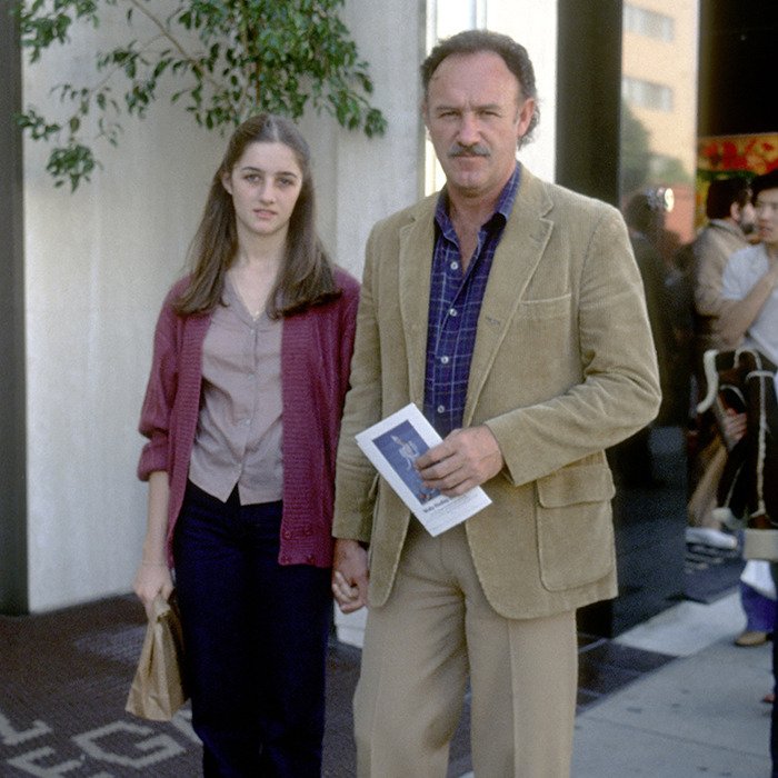 A man and a young woman holding hands on a sidewalk, near a potted plant, outside a building.