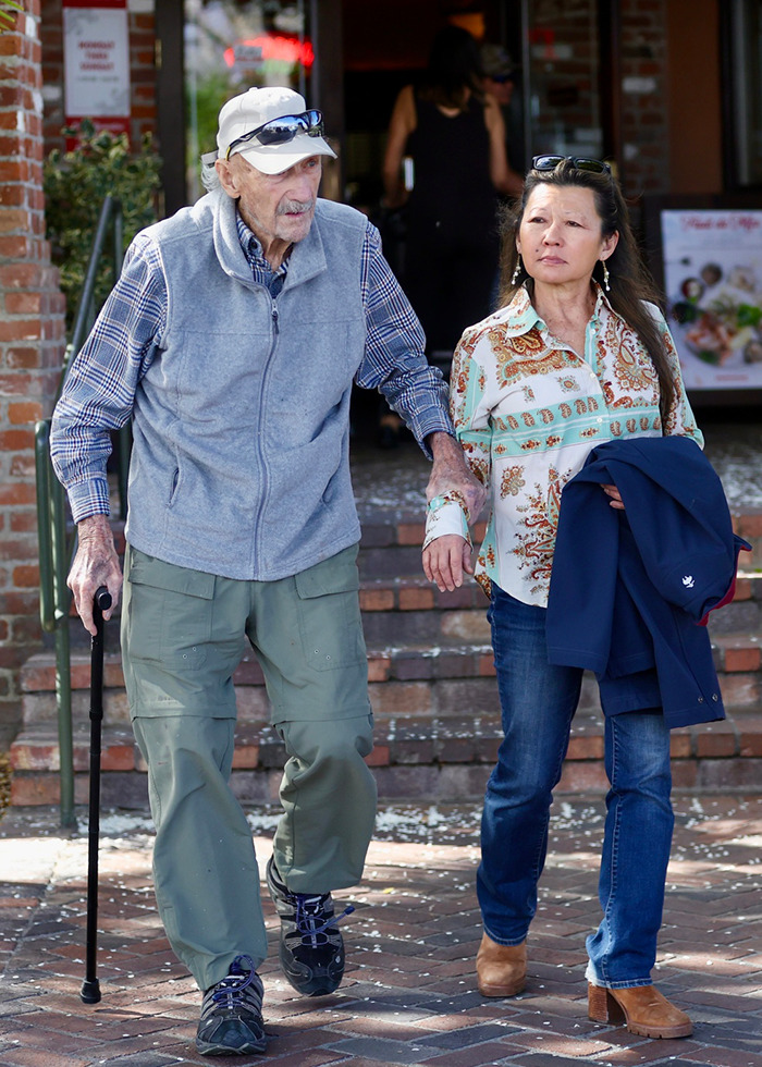 Elderly man with a cane and a woman walking outdoors, reflecting a strict diet and exercise regime.