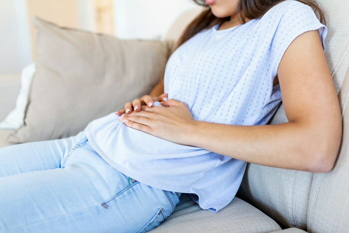 Woman in a blue shirt holding her stomach, representing niche facts about the female body.