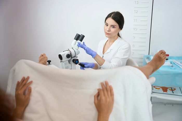 Doctor in a lab coat conducting a gynecological exam with a microscope, highlighting niche facts about the female body.