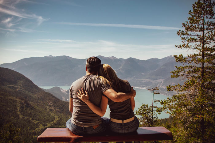 Couple sitting on a bench, overlooking a scenic mountain and lake view, illustrating themes of relationship and companionship.