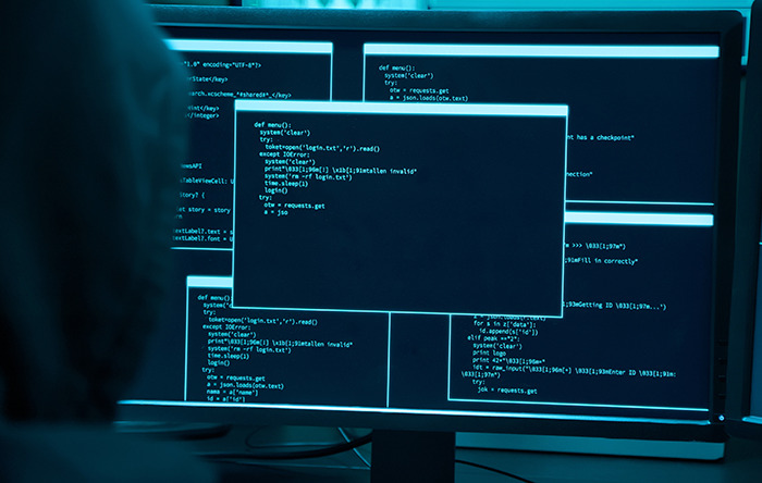 Stock photo of hacker in front of computer screen showing code.