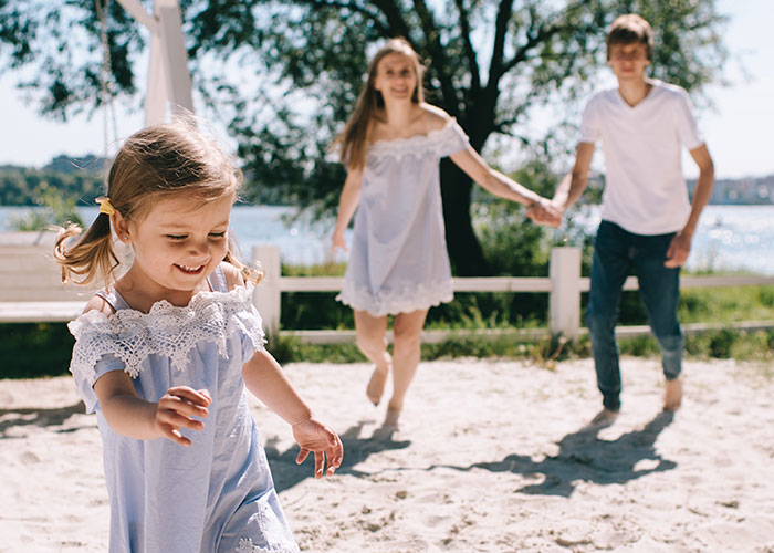 Family playing on a sunny beach, little girl running ahead, evoking emotions linked to husband's heartbreak.