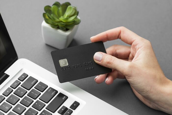 Hand holding a black card near a laptop, symbolizing travel must-haves.