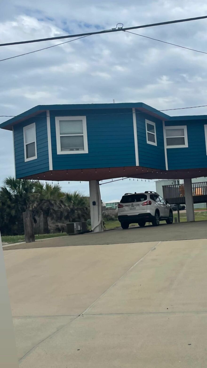 Unusual architecture of a blue house elevated above the ground with a car parked underneath.