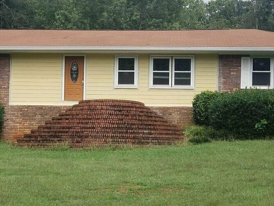 A yellow house with an unusual brick staircase, illustrating architecture shaming for its impractical design.