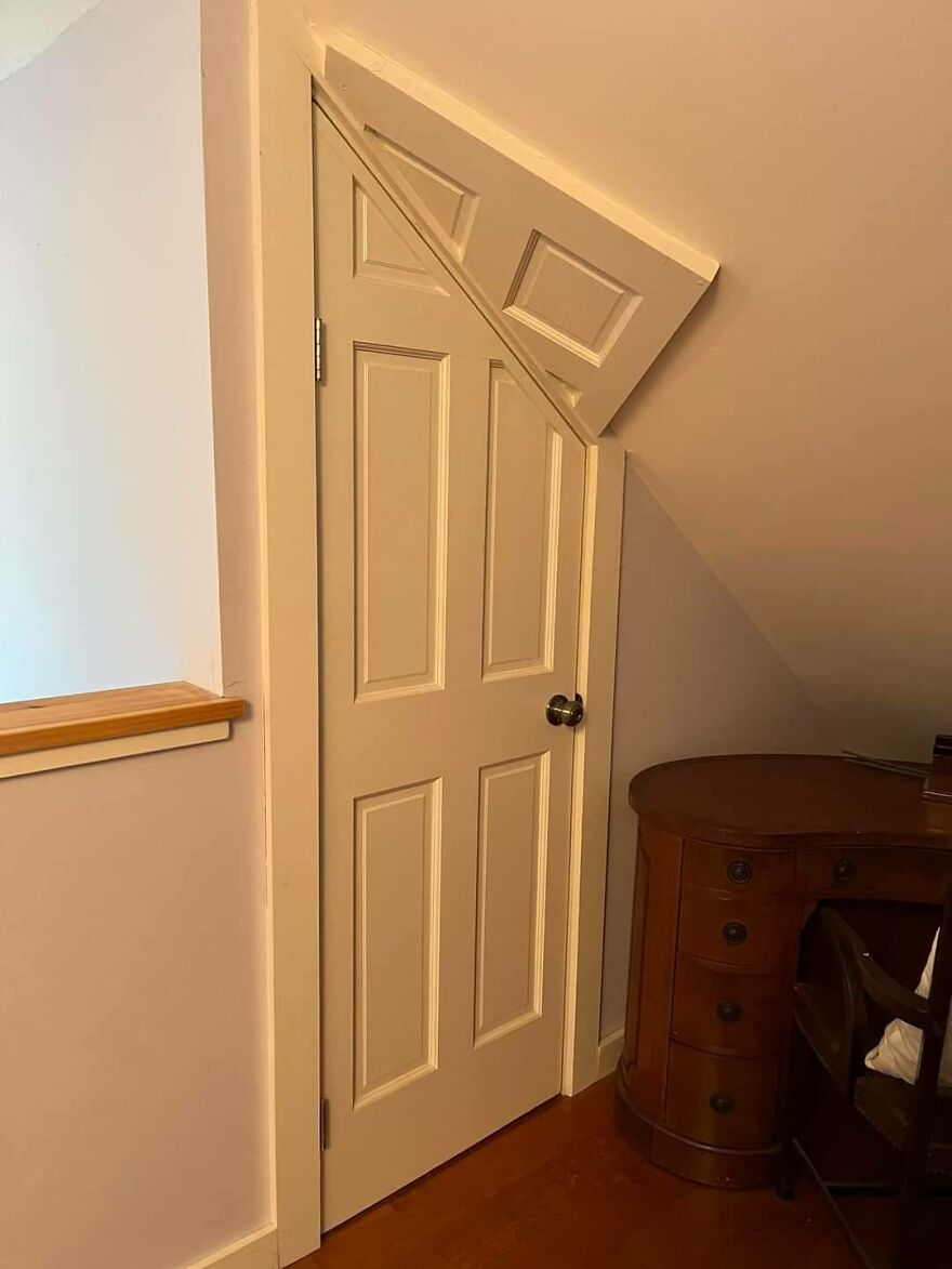 Oddly cut door under a slanted ceiling, showcasing architecture shaming in a room with a wooden desk.