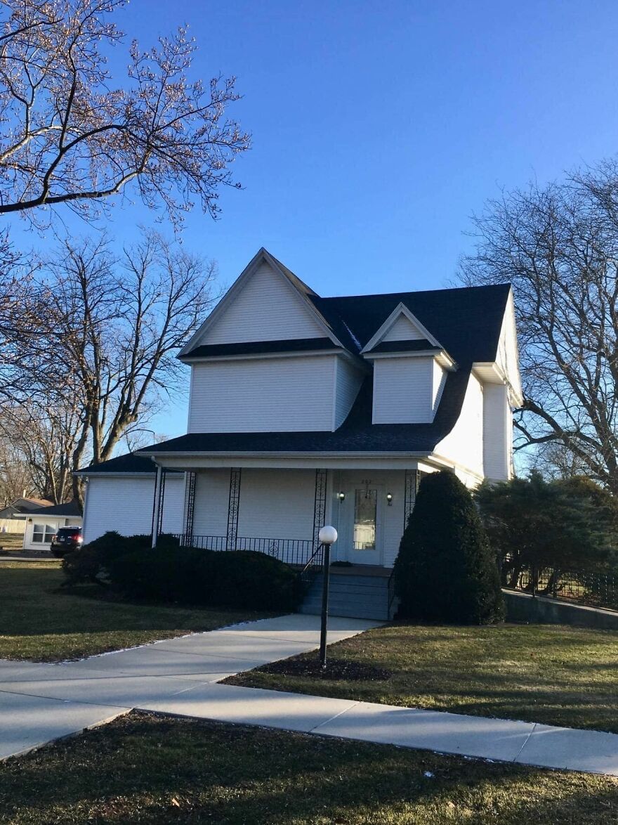 Oddly designed house with misaligned roof, surrounded by trees and clear blue sky, illustrating architecture shaming.