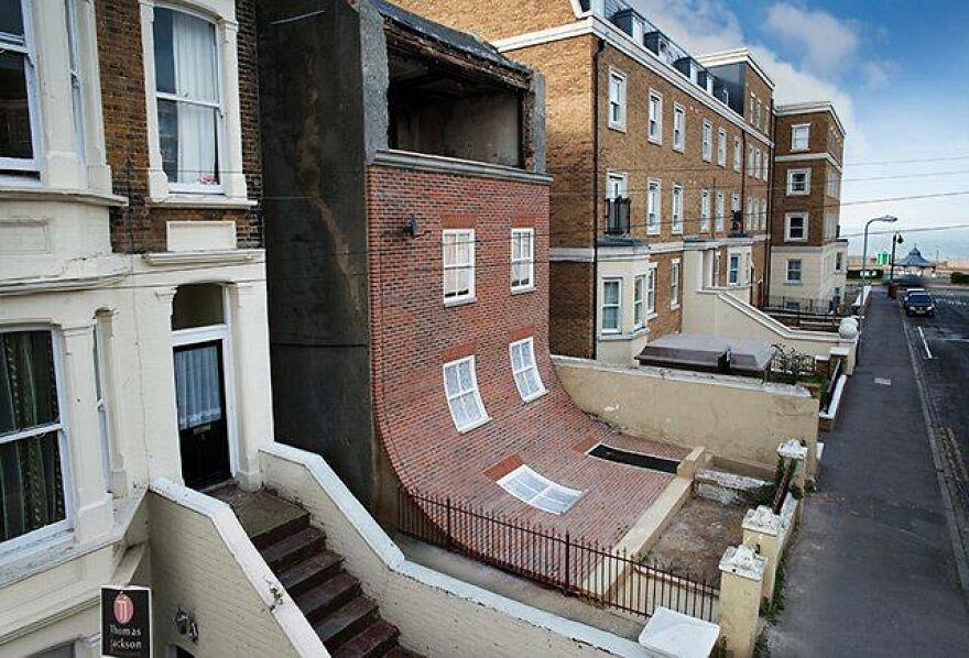 A warped, sloping brick building, illustrating architecture shaming for bizarre design on an urban street.