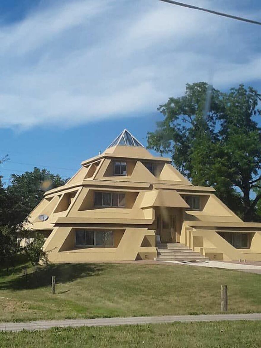 Pyramid-shaped yellow building, showcasing unique architecture on a grassy lawn.