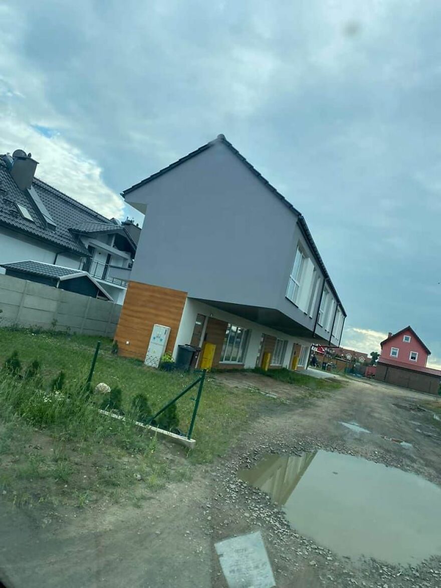 Awful architecture: a building with an oddly tilted structure stands on a muddy plot with overcast skies.