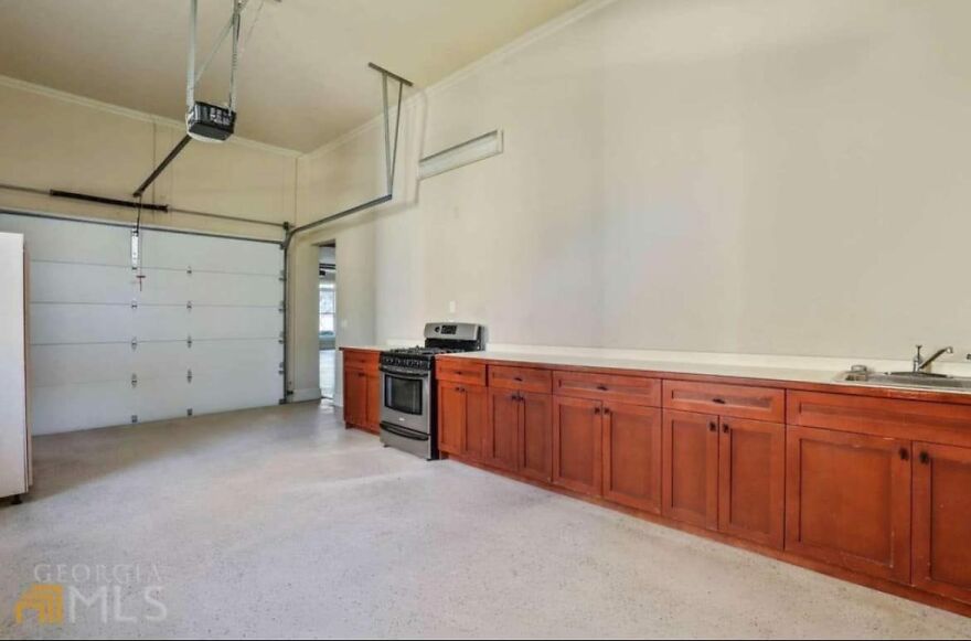 Odd architecture with a kitchen inside a garage, featuring wooden cabinets, a stove, and a sink.