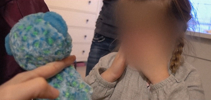 Blurred child holding hands to face, being offered a blue teddy bear, related to momfluencer abuser docuseries.