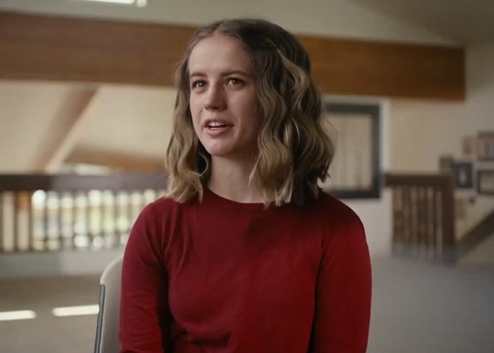 Person in a red shirt sitting in a room, featured in a docuseries about momfluencer abuse.