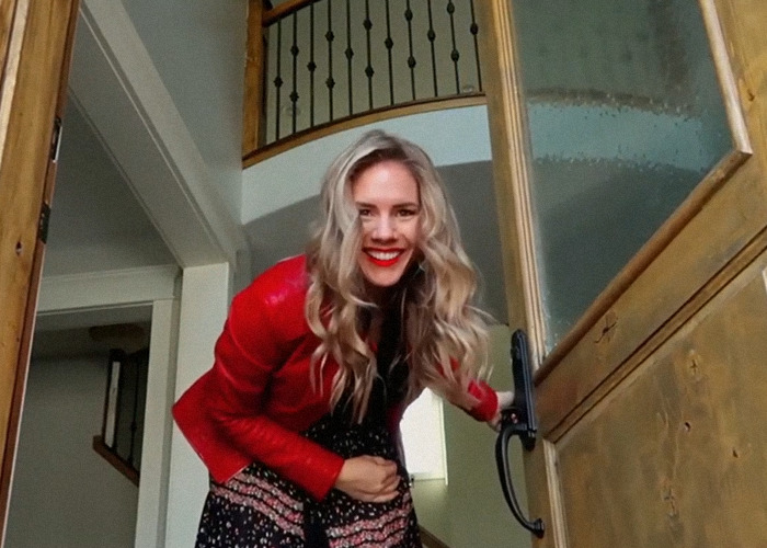 A woman in a red jacket smiling at the door, related to the docuseries about momfluencer misconduct.