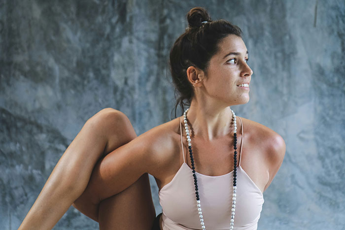 Woman practicing yoga with a serene expression, wearing a necklace and tank top, embodying a moment of calm and focus.