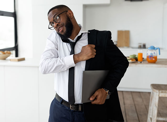 Man in a suit adjusting jacket, holding a laptop, in a modern kitchen.