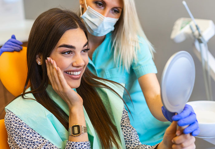 Woman smiling at her reflection in a dentist's chair, feeling grateful.