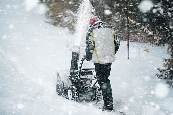 Man using a snow blower in snowy driveway during winter weather.