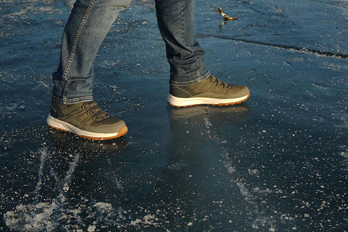 Boots walking on icy driveway surface, shimmering under sunlight.