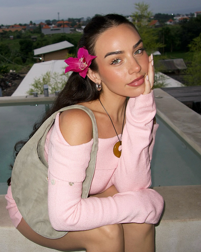 Influencer wearing a pink dress by a poolside with a flower in her hair, showcasing "wetlook" fashion.