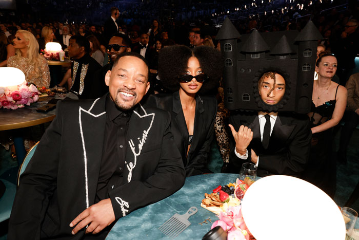 People at a table dressed for the Grammys 2025, including a person in a castle-themed headpiece.