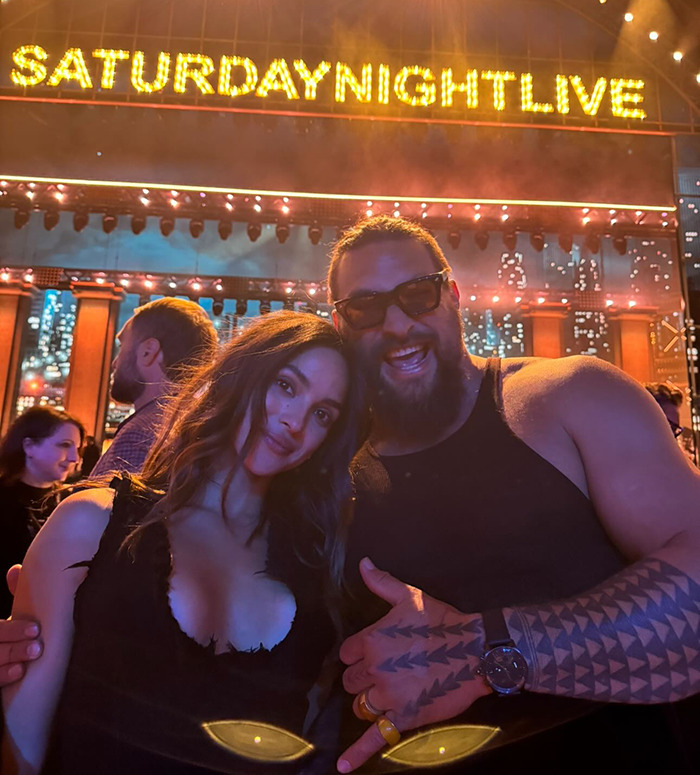 Jason Momoa at Saturday Night Live event with his new girlfriend, posing with a smile under marquee lights.