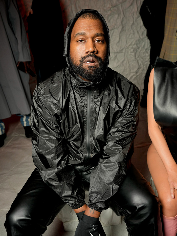 Kanye West in a black outfit sitting indoors.