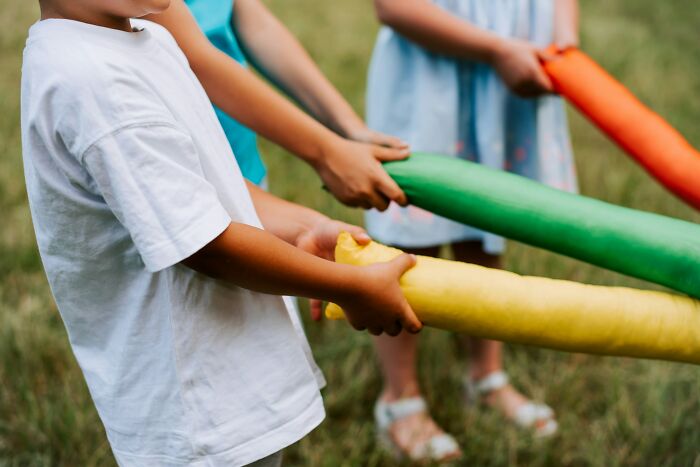 Children holding colorful foam cylinders outdoors, representing playful teamwork.