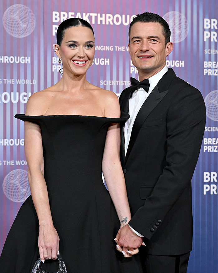 A woman in a black dress and a man in a tuxedo holding hands at a formal event.