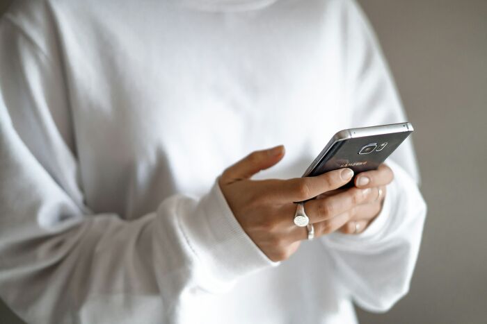 Person in a white sweater using a smartphone, illustrating Gen Zers expressing their "Boomer complaints."