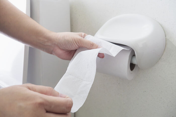 Hands pulling a sheet from a wall-mounted toilet paper dispenser, highlighting travel must-haves.