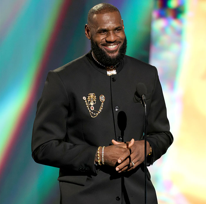 Man in formal black attire smiling at the Met Gala, amid discussions on the event's dress code and celebrity hosts.