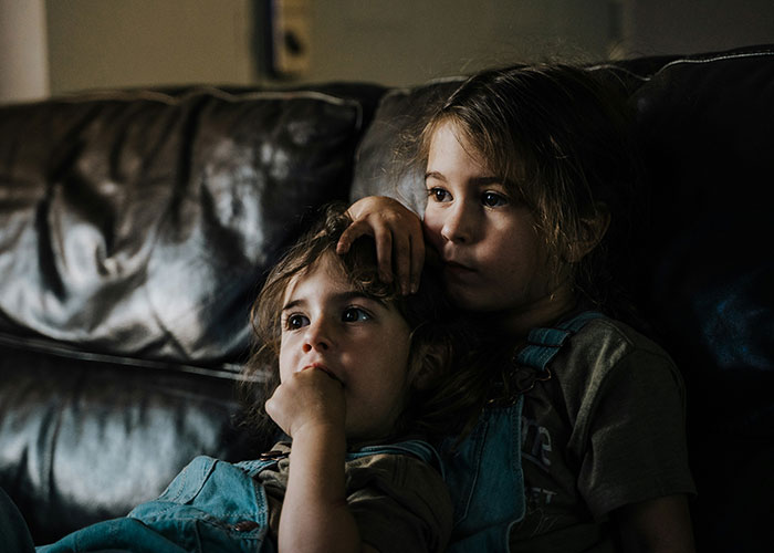 Children sitting on a couch in a dimly lit room, looking thoughtful.