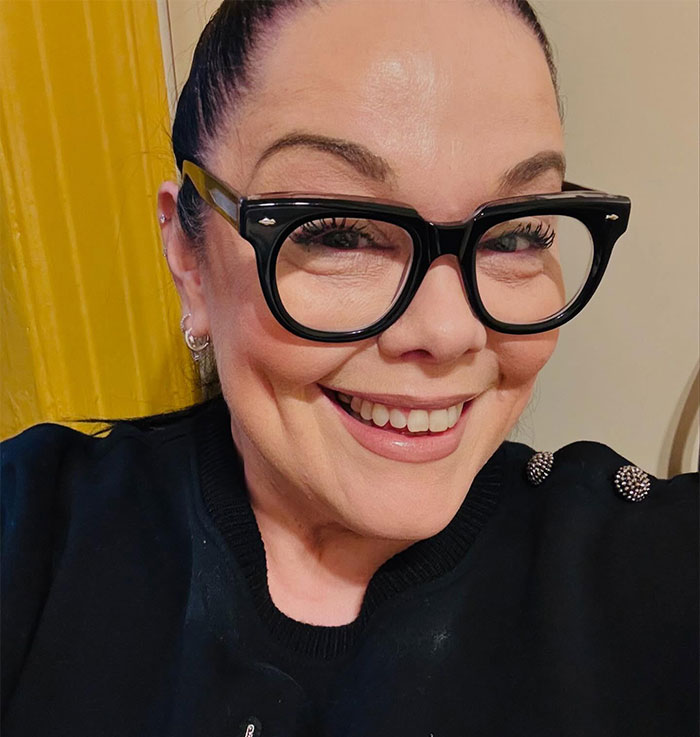 A person smiling, wearing large black glasses, related to celebrity criticism of Bianca Censori's Grammys dress.