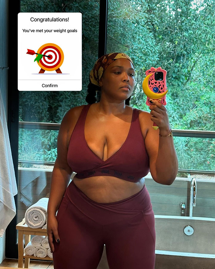 Woman in maroon workout outfit taking a mirror selfie indoors, showing off a slimmer figure.