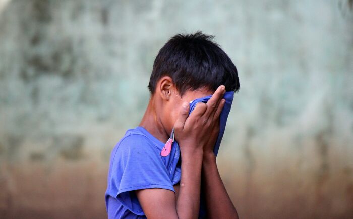 Child in a blue shirt wipes face with a cloth, offering a fresh perspective on everyday life.