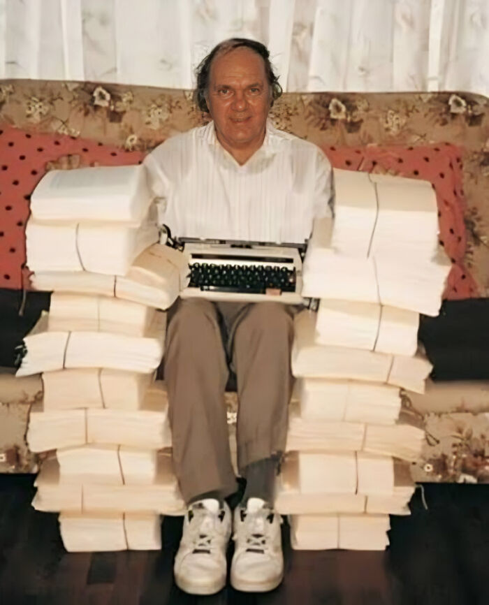 Man seated amidst stacks of paper with a typewriter, illustrating random world facts in a fresh perspective.