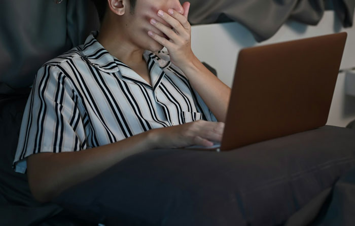 Man in striped pajamas looking shocked while using a laptop, expression of surprise.