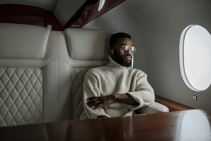 Man in a white sweater sitting beside an aircraft window, looking contemplative.