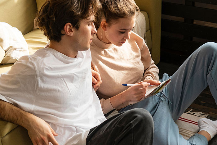 Young couple sitting together on a couch, discussing notes, highlighting moving out to live with her boyfriend.