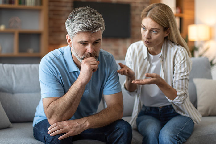 Man and woman having a serious conversation on a couch, emotions tense, discussing living arrangements with stepdad.