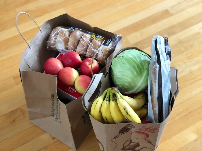 Paper grocery bags filled with apples, bananas, cabbage, and rolls on a wooden floor; represents Gen Zers' lifestyle habits.