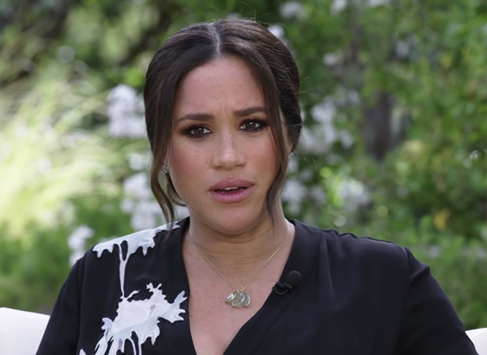 Meghan Markle wearing a black and white top, looking surprised in a garden setting outdoors.